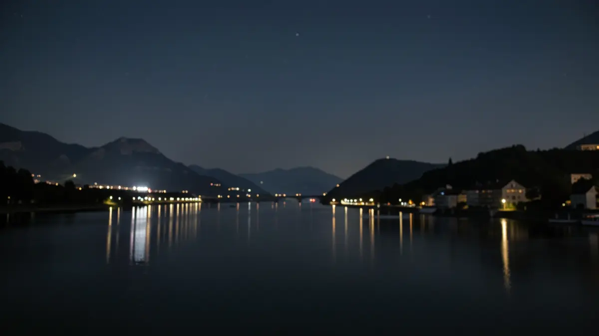 Ciel nocturne au-dessus d'un plan d'eau, avec quelques lumières douces au loin.