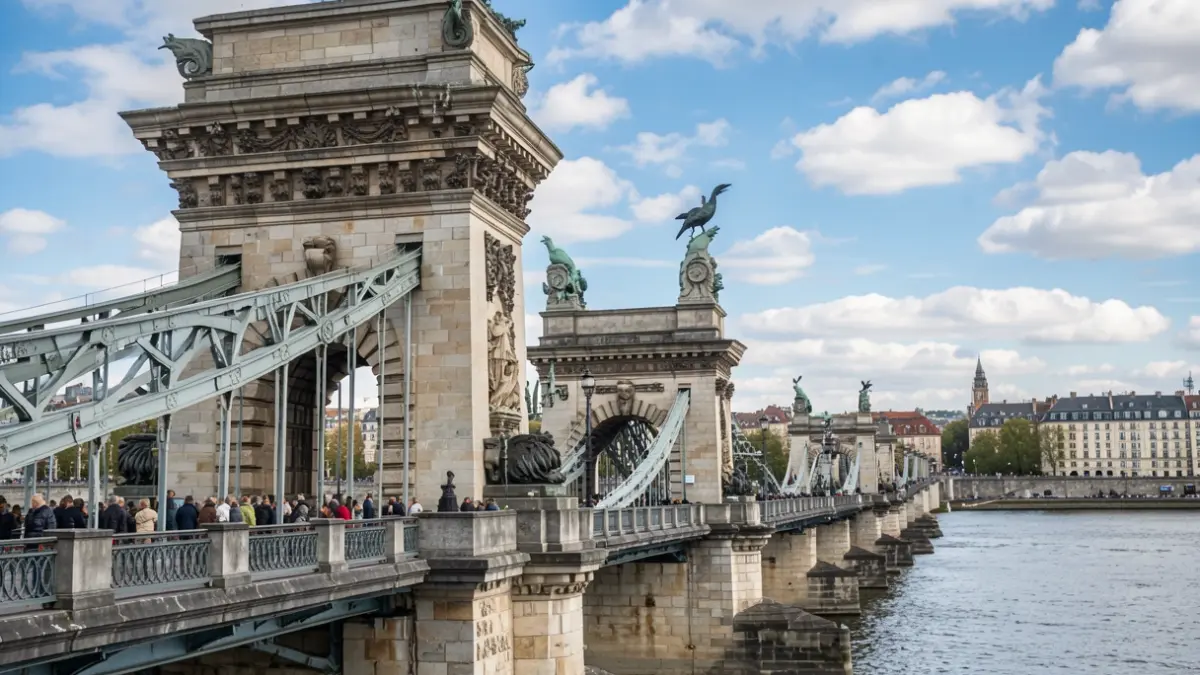 Generic image of a historic stone bridge facade with ornate architectural details, including pylons and bronze roosters, under a blue sky with scattered clouds. The bridge spans a wide river, with blurred city buildings in the background.